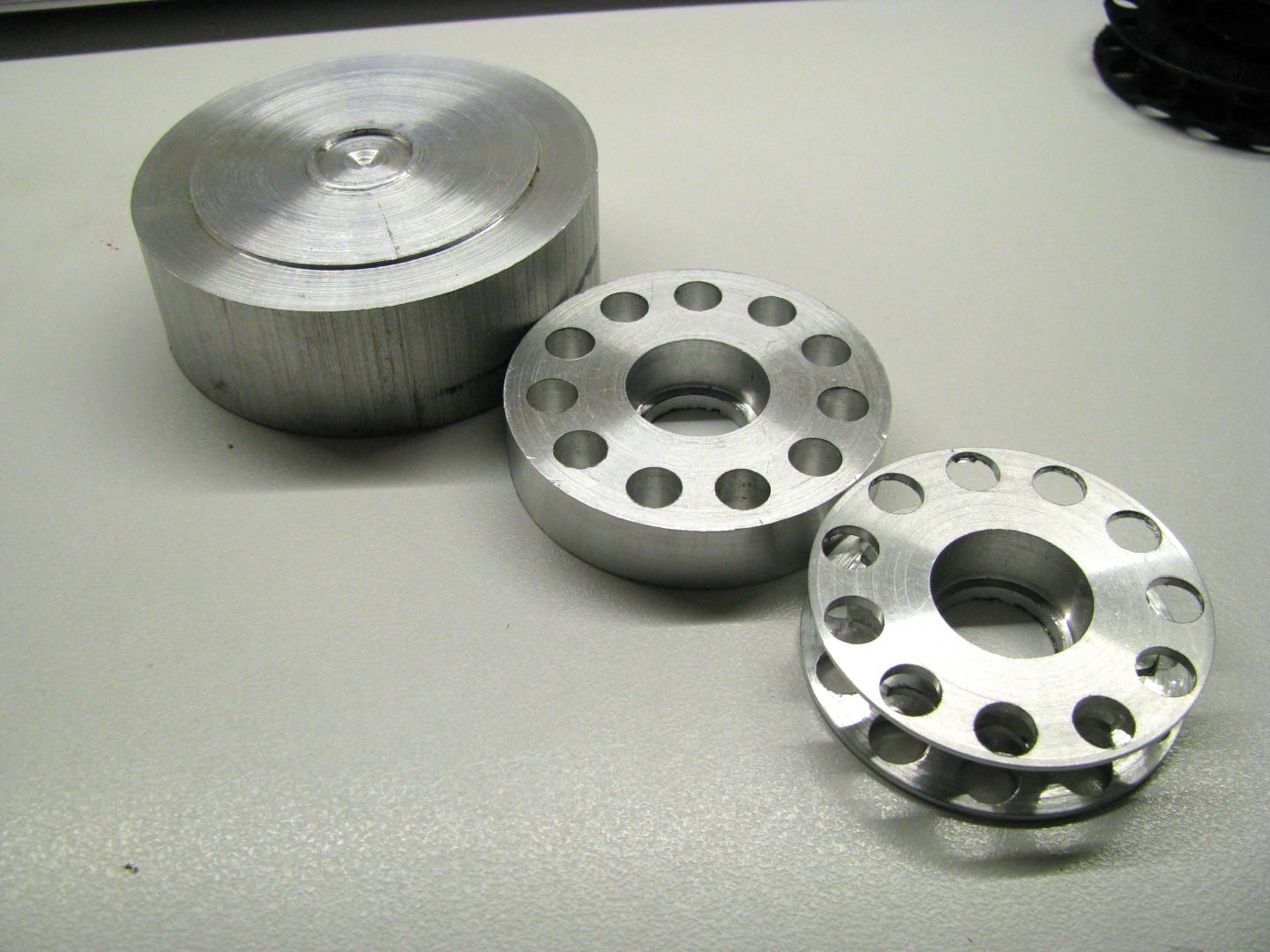 A finished idler sprocket next to a partially completed one and the stock material they were made from.